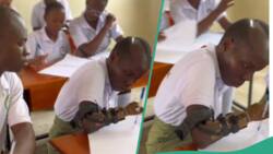 Young girl with prosthetic hands writes with it in front of her colleagues in class
