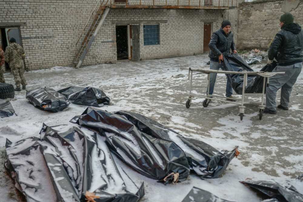 Two men carry a corpse in a body bag to lay it next to others in a snow covered yard in  Mykolaiv, a city on the shores of the Black Sea that has been under Russian attack for days, on March 11, 2022