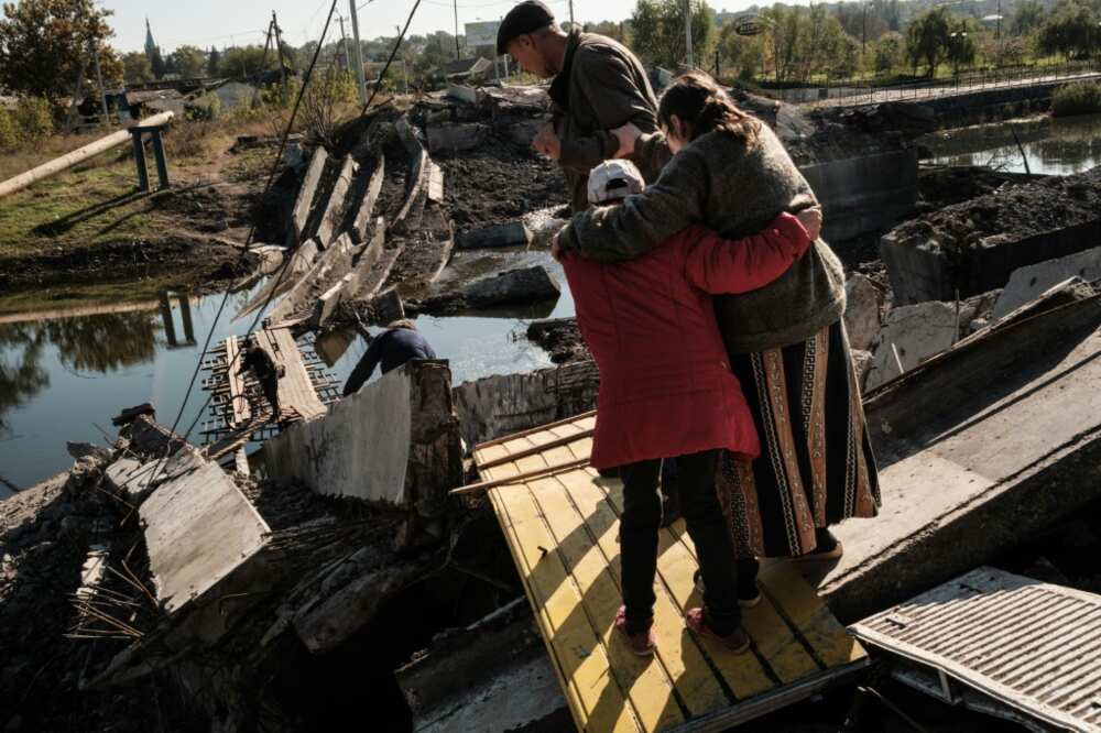 Disabled Bakhmut resident, Rimma Tsykalenko, 65, is helped by neighbours to cross a destroyed bridge on the way to her home after receiving her monthly pension payment