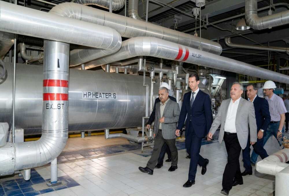 A handout picture released by the Syrian Presidency Facebook page on July 8, 2022, shows Syria's President Bashar al-Assad (C) touring a thermal power station in the eastern countryside of Aleppo province
