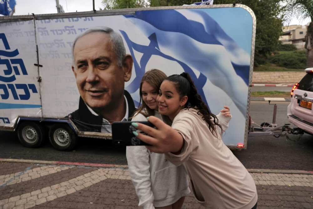 Two girls pose for a selfie photo before a vehicle showing Israel's former prime minister Benjamin Netanyahu, ahead of November 1 general elections