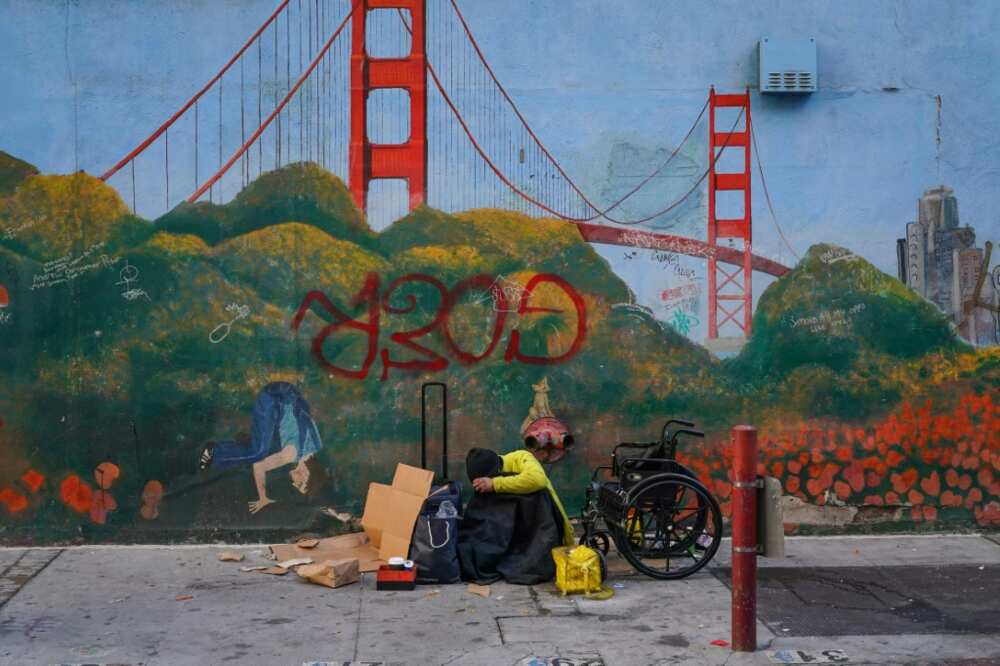 A homeless person leans against a mural of the Golden Gate Bridge near APEC Summit headquarters in San Francisco, California on November 11, 2023