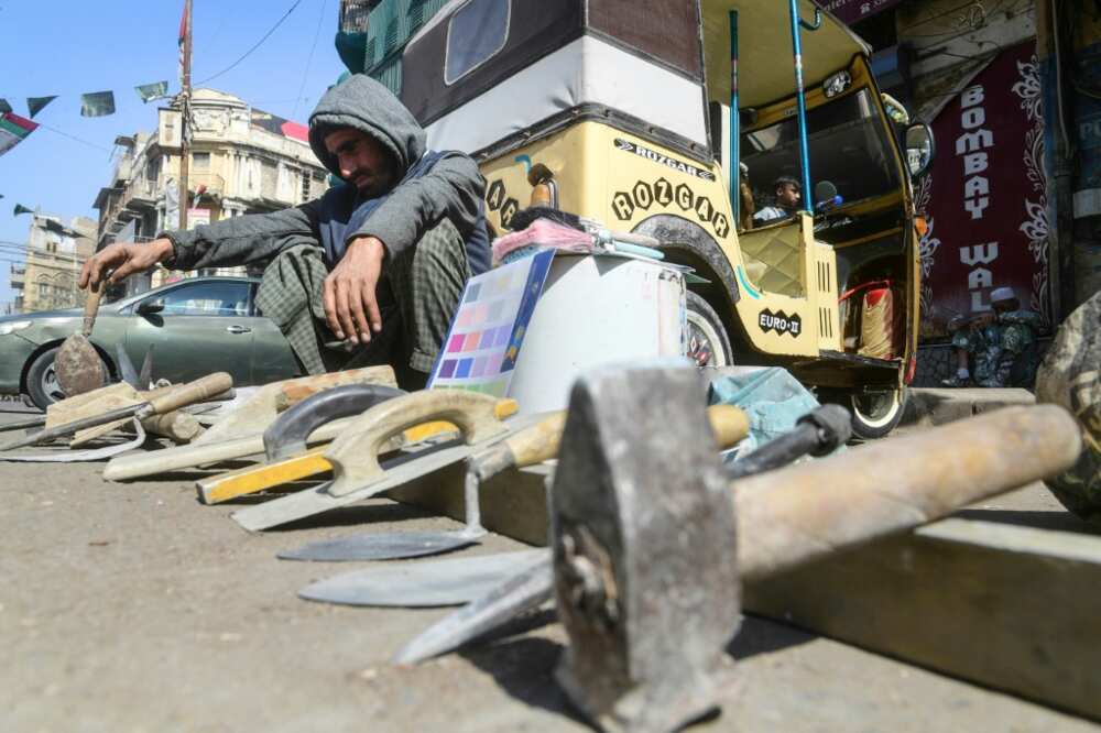 Day labourers, their tools laid out in front of them, wait for work that never comes along a road in Karachi