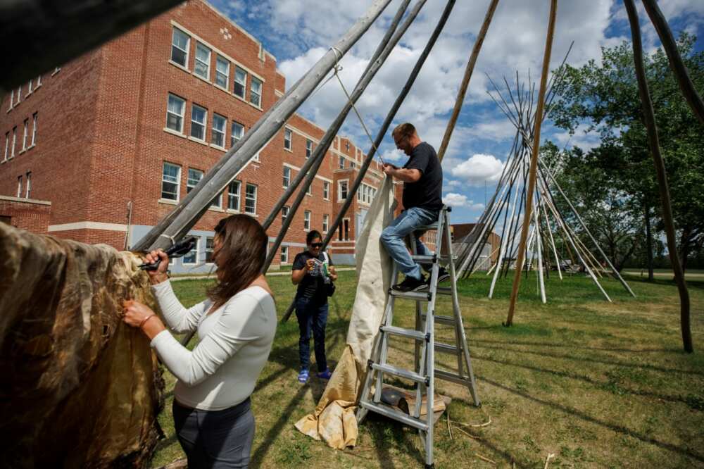Jay Williams (C), of Saddle Lake First Nation, climbs atop a ladder as he and Joi Arcand attach a moose hide to a teepee outside the University nuhelt'ine tahiyots'i nistameyimakanak Blue Quills in St Paul, Alberta, Canada