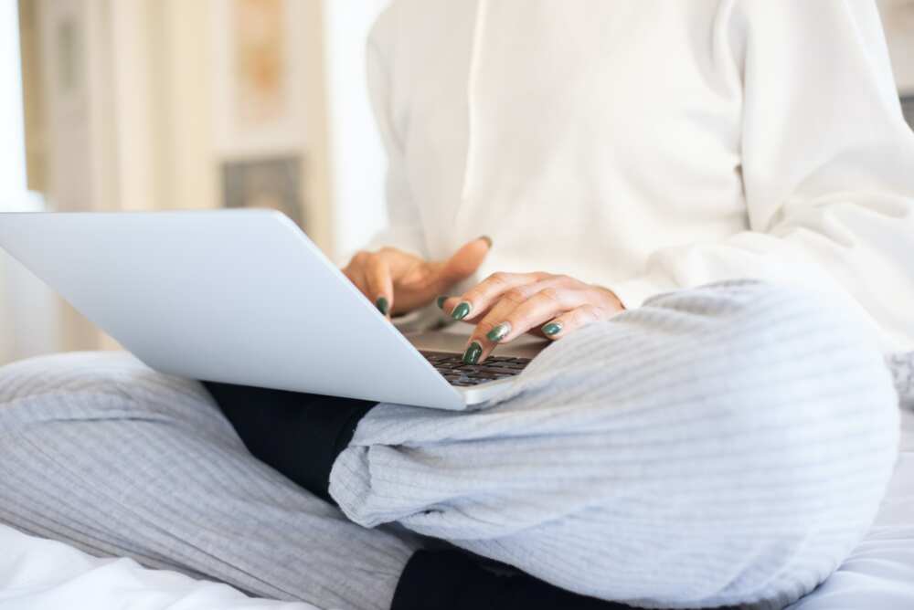 Close-up shot of a person in white using a laptop while sitting on a bed.