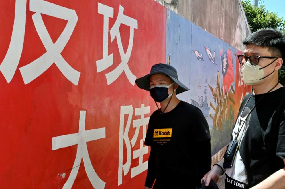 Tourists on Taiwan's Kinmen islands walk past a mural with a slogan that reads 'seize mainland China'