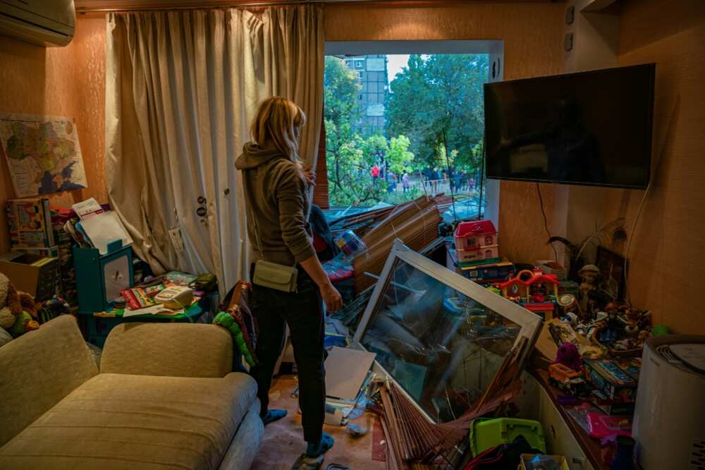 A woman looks out of a broken window of a damaged apartment