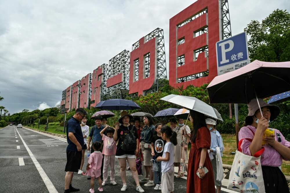 People in Xiamen wait for a bus on a street next to a sign that reads in Chinese "One country, two systems: reunify China"