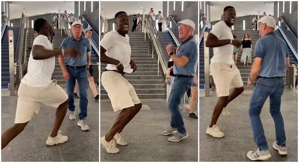Black man and white man dancing in front of a busy elevator.