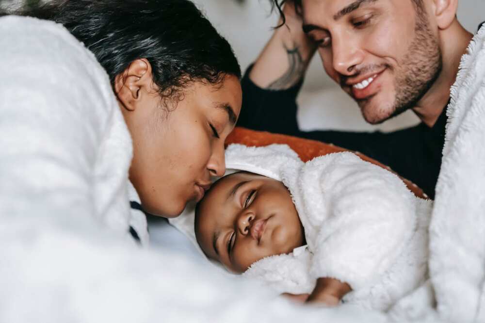 A couple sleeps with their kid on the bed