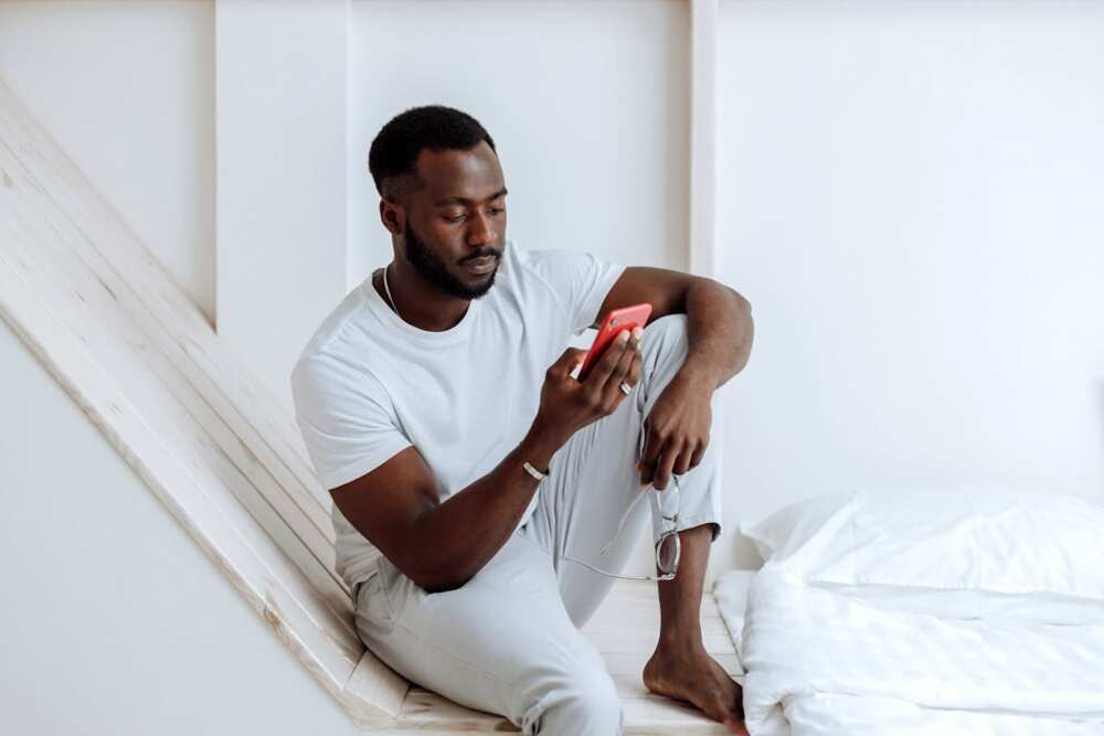 A man using a phone while sitting on a white surface