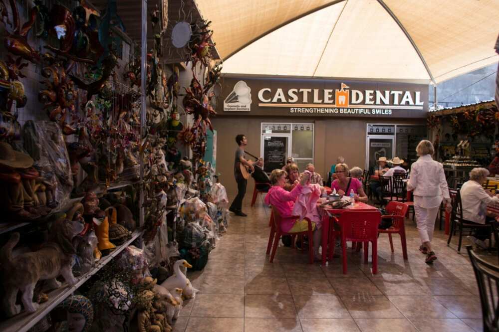 In this photo taken on February 15, 2017 visitors from the United States sit near a souvenir stand and dental clinic in downtown Los Algodones, near the US/Mexico border, northwestern Mexico