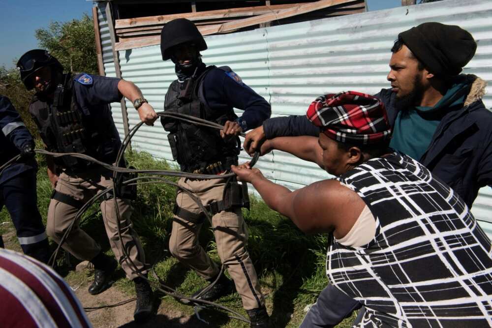 Cape Town police try to prise an illegally connected electricity cable from residents of an informal settlement Cape Town police try to prise an illegally connected electricity cable from residents of an informal settlement