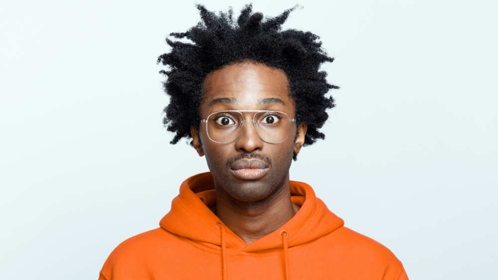A young man wearing an orange hoodie and glasses staring at someone