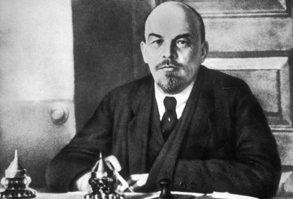 Vladimir Lenin sitting at a table in a black suit and a white shirt