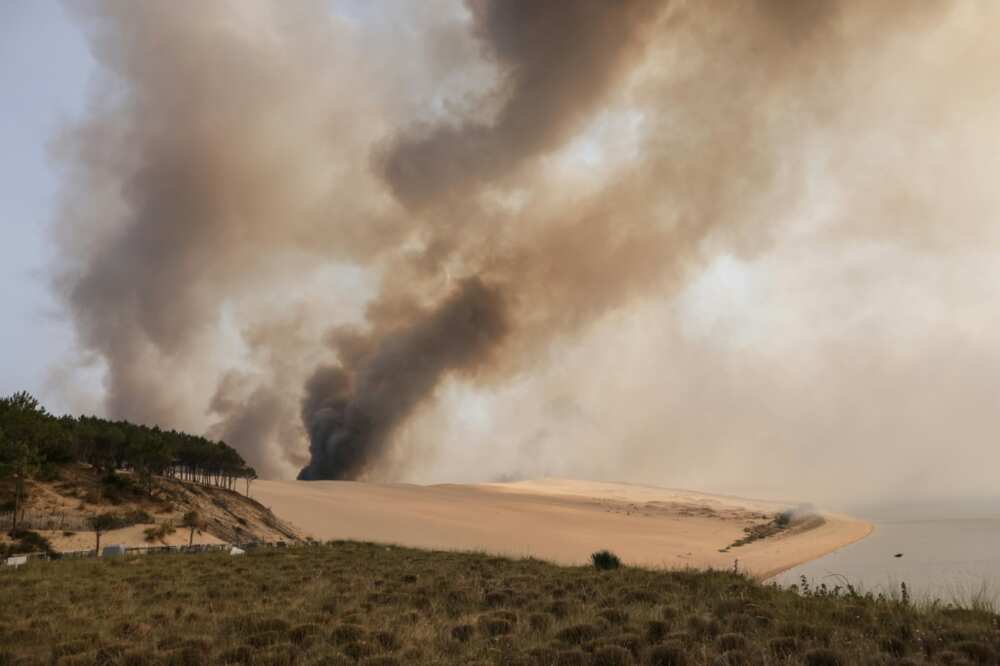This photograph taken on July 18, 2022 shows the smoke rising from the forest fire in La Teste-de-Buch, seen from Pyla sur Mer, in front of the Pilat dune.  In scorching heat, with more than 40°C, some 8,000 people had to leave - in a "preventive manner" according to the prefecture - the Miquelots and Pyla-sur-Mer, districts of the municipality of La Teste-de-Buch, a town of 28,000 inhabitants where 4,300 hectares of forest went up in smoke.