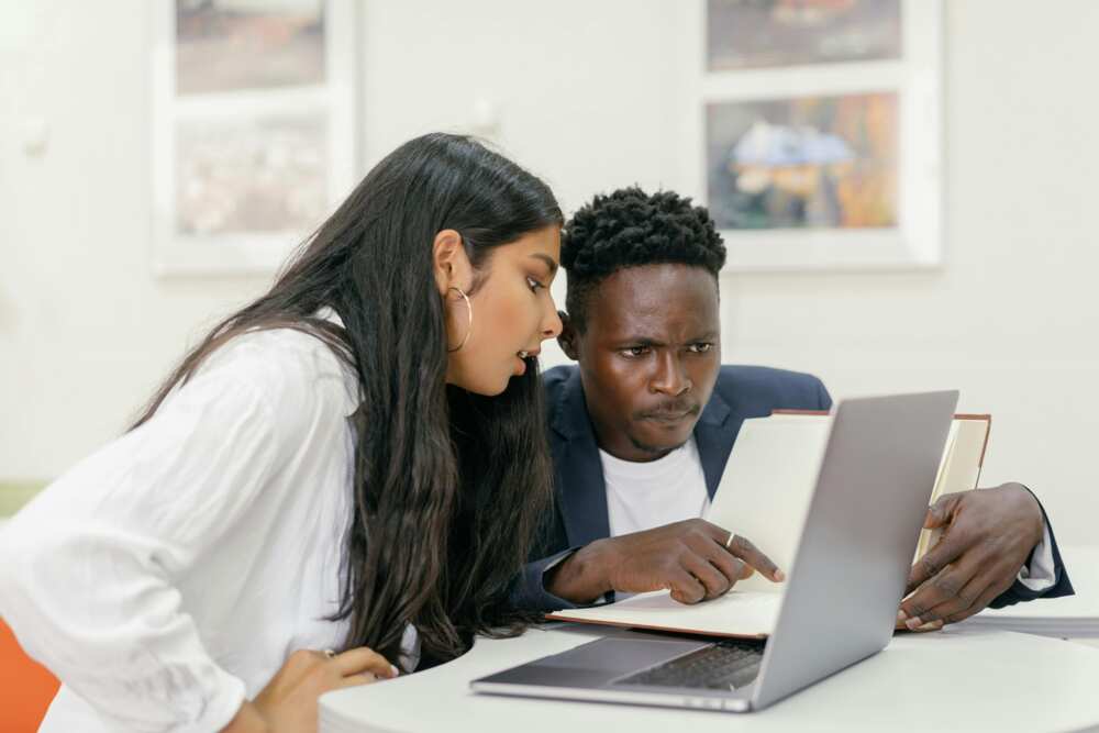 A professor and a student sitting at a desk with a computer and a book