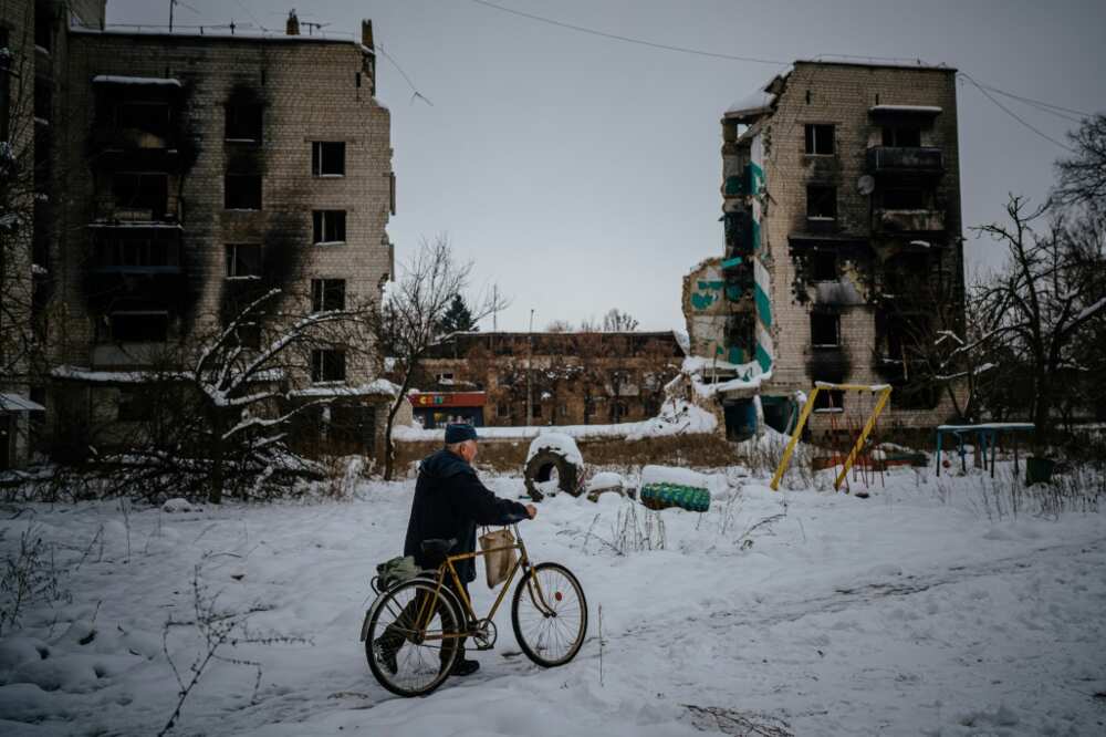 A resident of Borodianka pushes his bike on a snow covered street next to destroyed residential buildings