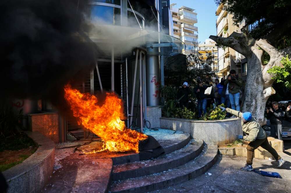 A protester throws a brick at a bank after setting fire to tyres during a demonstration in Beirut