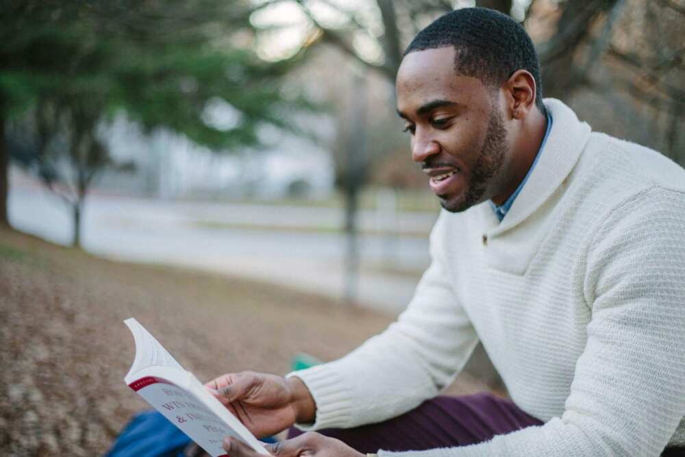 A man in a white sweater reading a book