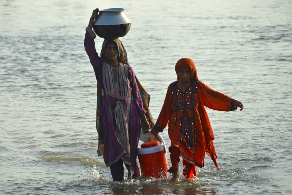 Girls wade through floodwater while carrying drinking water in Jaffarabad, Balochistan