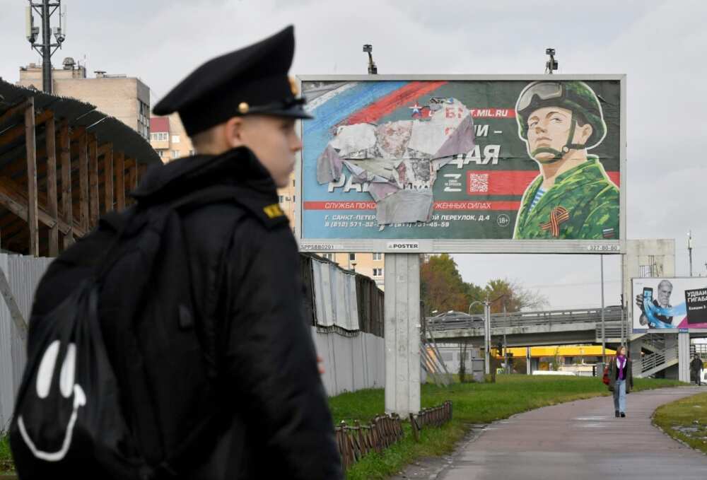 A military cadet stands in front of a billboard promoting contract army service in Saint Petersburg