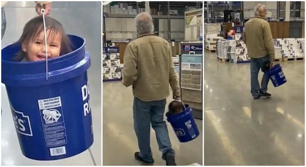 The man carries the baby inside a blue bucket while strolling in a store.