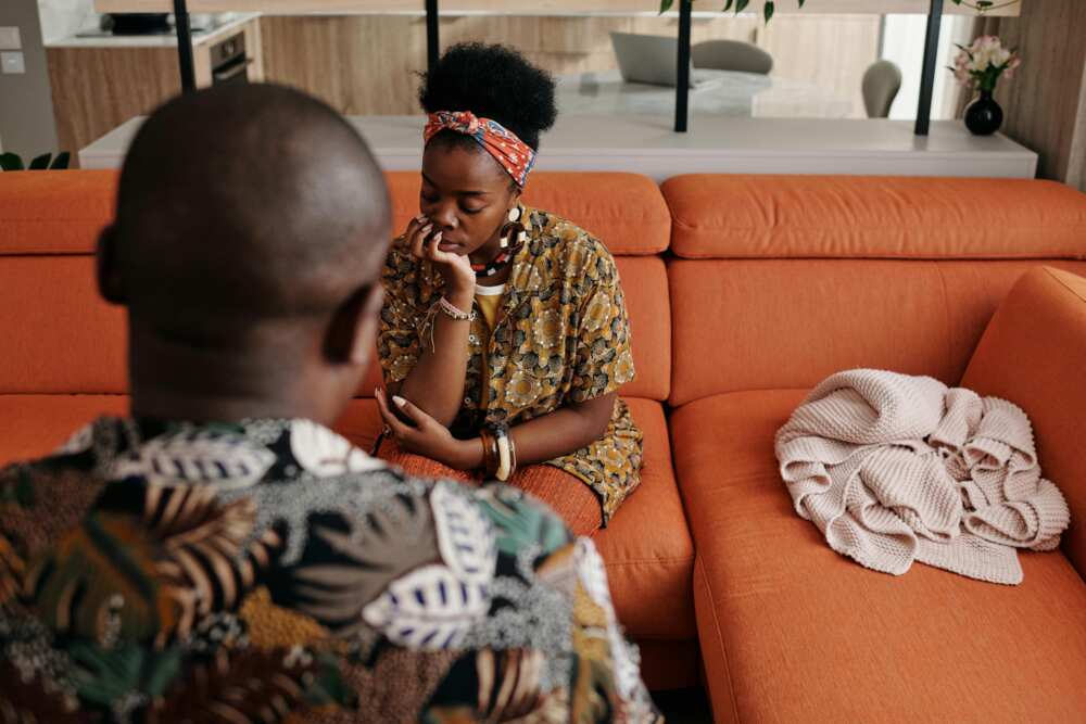 A man is having a conversation with a woman sitting on an orange sofa.
