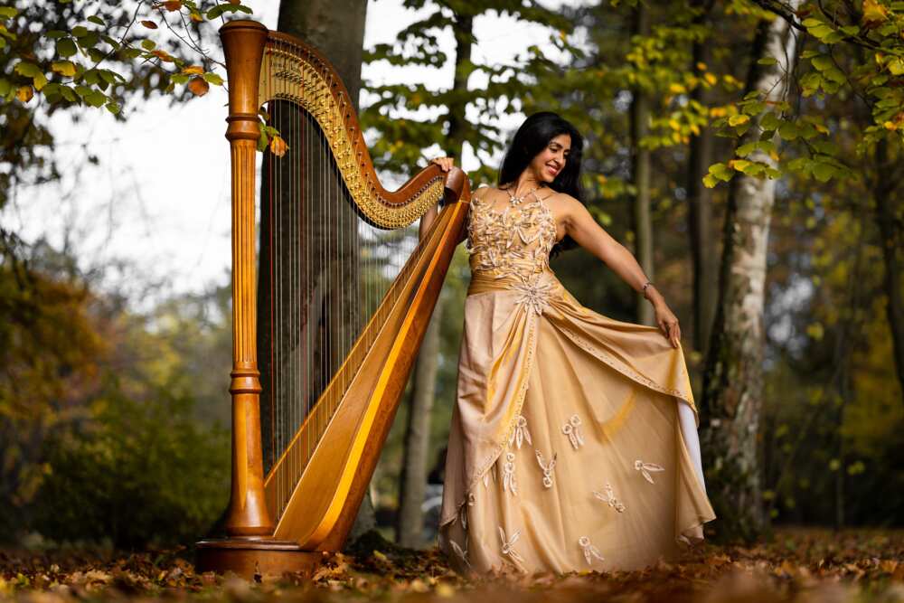 A woman posing with a harp in the forest