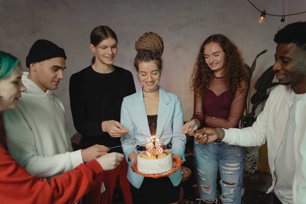 A group of young people at a party lighting sparklers on candles on top of the cake.