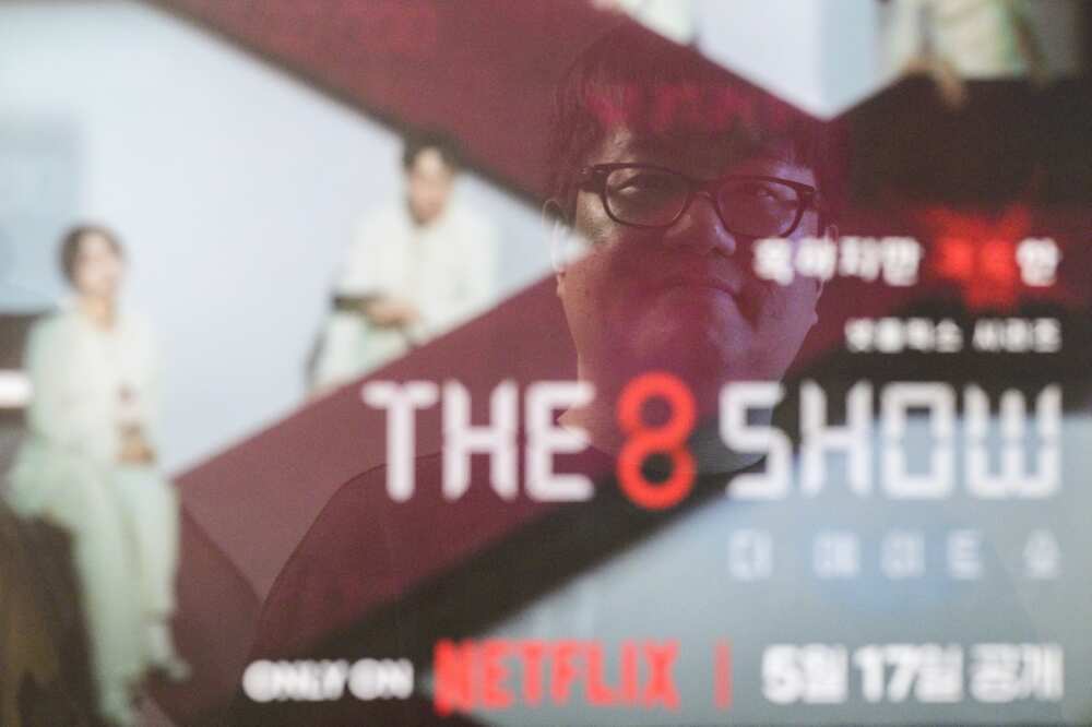 Bae Jin-soo, who created the Naver webtoons "Money Game" and "Pie Game" which inspired Netflix's "The 8 Show", poses in front of a framed poster for the show