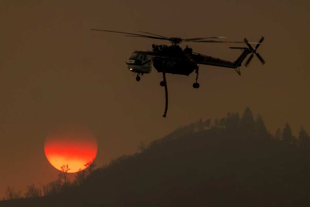 A firefighting helicopter passes the setting sun while fighting the Oak Fire near Mariposa, California